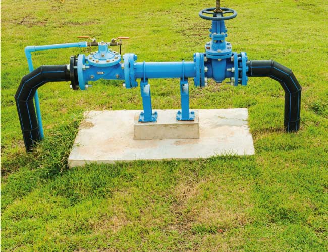 Side view of a blue commercial irrigation backflow prevention system connected to underground piping, demonstrating a code-compliant installation on a concrete foundation.