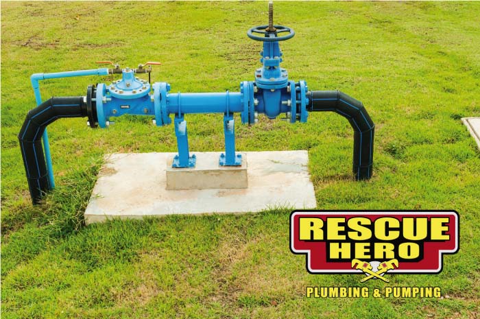 Bright blue industrial water control valve connected to black HDPE piping installed on a concrete pad in a grassy field, showcasing commercial plumbing infrastructure.