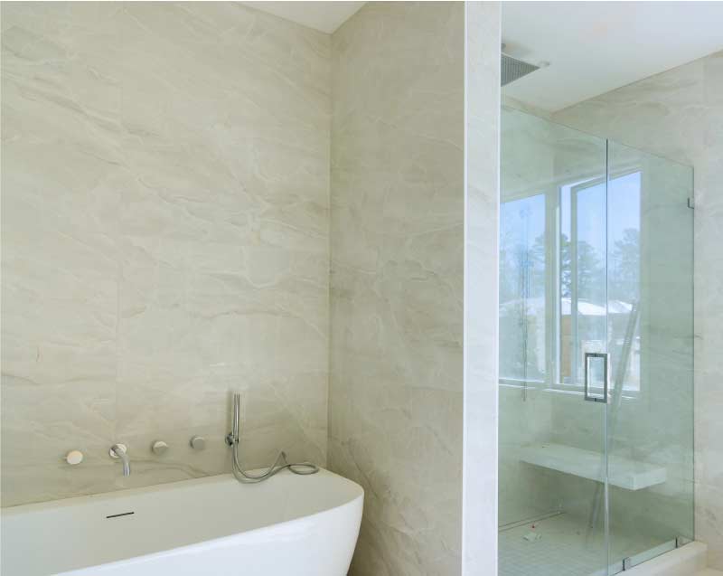 Bright, newly remodeled bathroom showcasing a sleek white bathtub, floor-to-ceiling marble-style tile work, and a custom glass shower door installation.