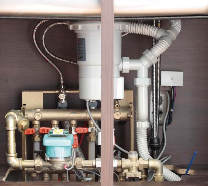 Complex under-sink plumbing configuration featuring a waste disposal unit, flexible drainage pipes, and a manifold system with shut-off valves inside a residential kitchen cabinet.