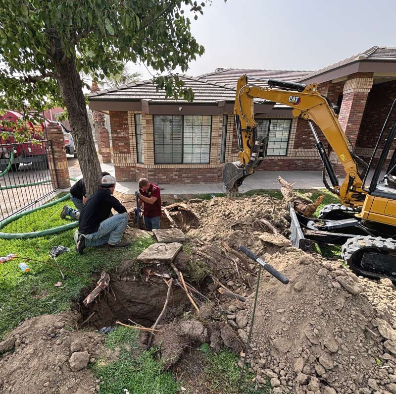 Crew of professional plumbers performing an underground sewer line excavation in a residential yard using shovels and a yellow mini-excavator, with a red service truck parked on the street for professional plumbing installation