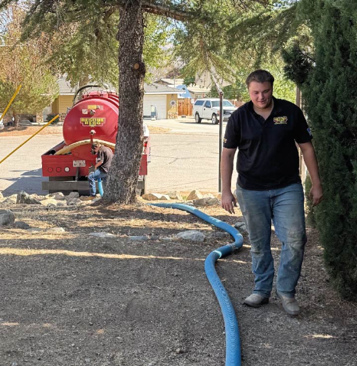 A Rescue Hero Plumbing plumber in bodfish managing a blue suction hose during a professional septic tank pumping service for a residence