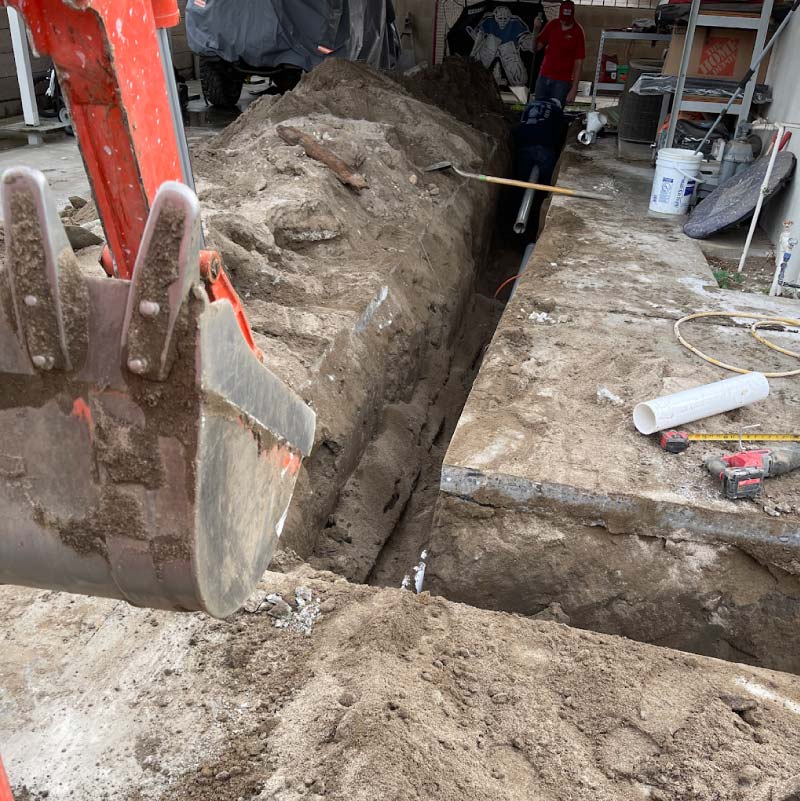 Close-up of a damaged water line pipe bursting beneath a cracked concrete foundation slab with visible water spray and moisture pooling, for Slab Leak Repair